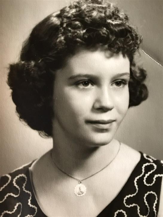 A young woman poses with a gentle smile, showcasing her vintage hairstyle and clothing in a studio.