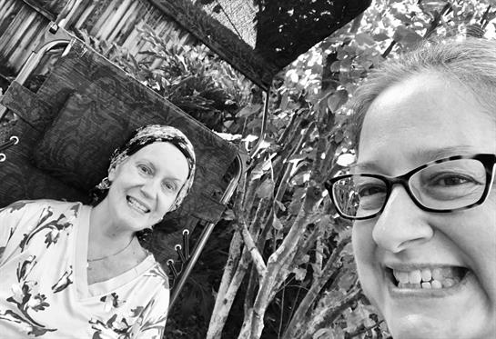 Two friends share smiles in a lush garden, surrounded by greenery and afternoon sunlight.