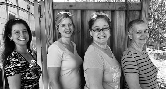Two women share a cheerful moment, posing with smiles outdoors at a casual gathering.