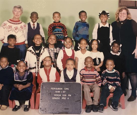 Kids and teachers pose for a 1990s-style school photo in the classroom.