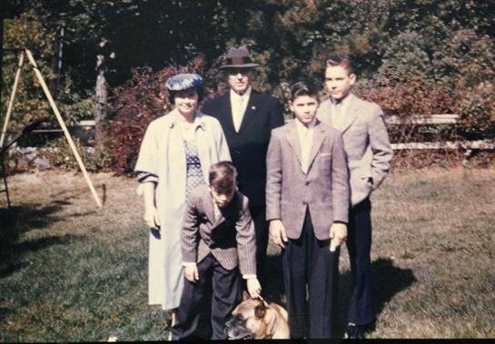 A family poses for a portrait in the backyard on a sunny day, dressed in vintage clothing.