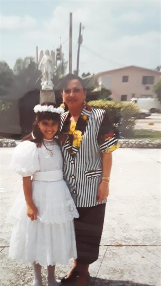 A young girl in a white dress stands beside an older man wearing a colorful patterned shirt.