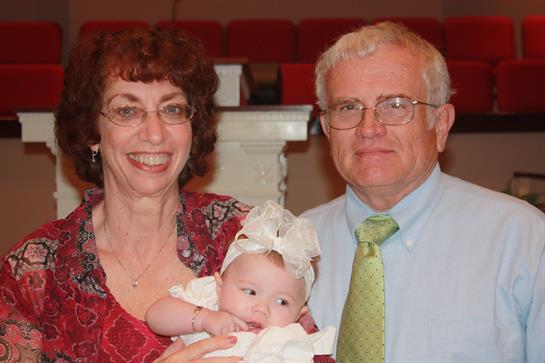 A couple enjoys a joyful moment holding their baby in a festive environment with smiles.