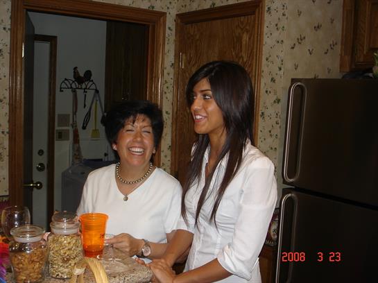 Two women share laughter while preparing snacks in a warm kitchen atmosphere.