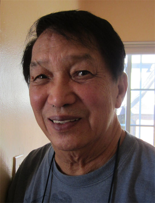 Elderly man with a warm smile stands indoors, enjoying a lively gathering with friends.