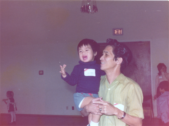 A father holds his child, who is joyfully expressing emotions, in a warmly lit indoor space.