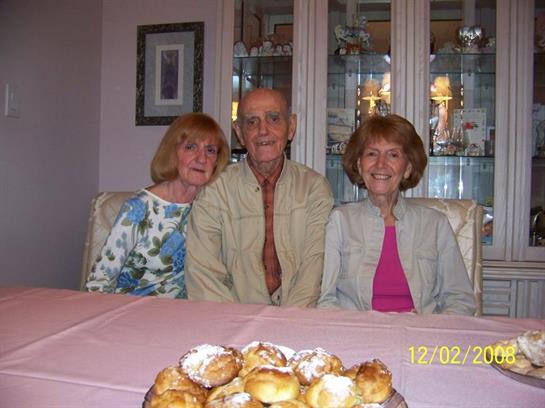Three friends sit together at a table adorned with pastries, enjoying a warm moment in their home.