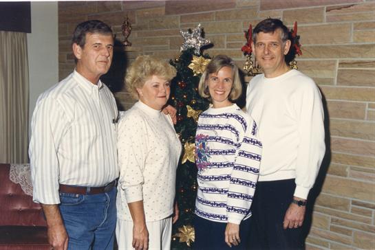 Four family members stand together, smiling, near a beautifully decorated Christmas tree.