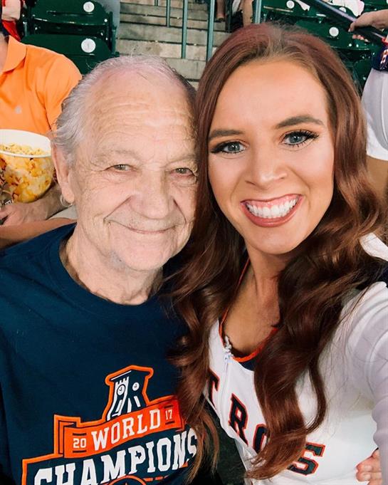 A young woman happily takes a selfie with her grandfather at a sunny outdoor family event.