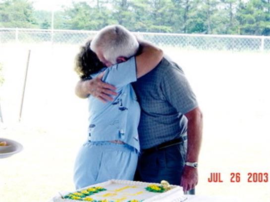 Two family members share a heartfelt hug at a summer gathering by a celebration cake.