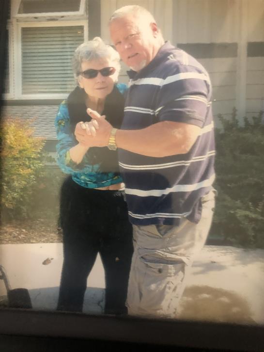A couple enjoys dancing together on a sunny afternoon outside their home, showcasing happiness.