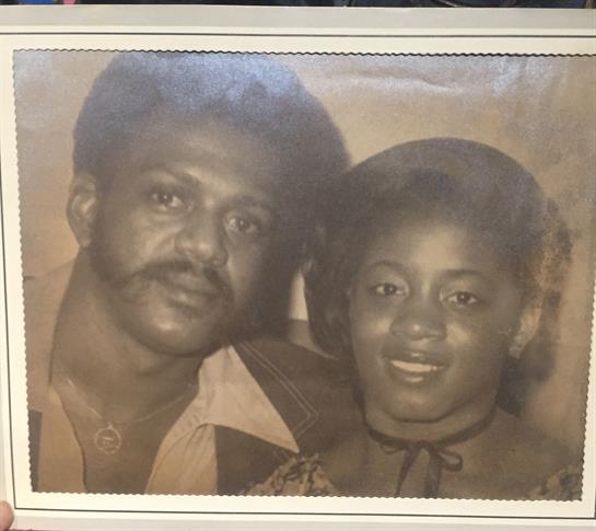 A couple poses closely together, both wearing vintage formal attire, exuding warmth and affection.