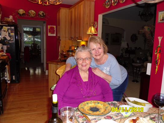 Two women enjoy each other's company in a warmly decorated kitchen during a gathering.