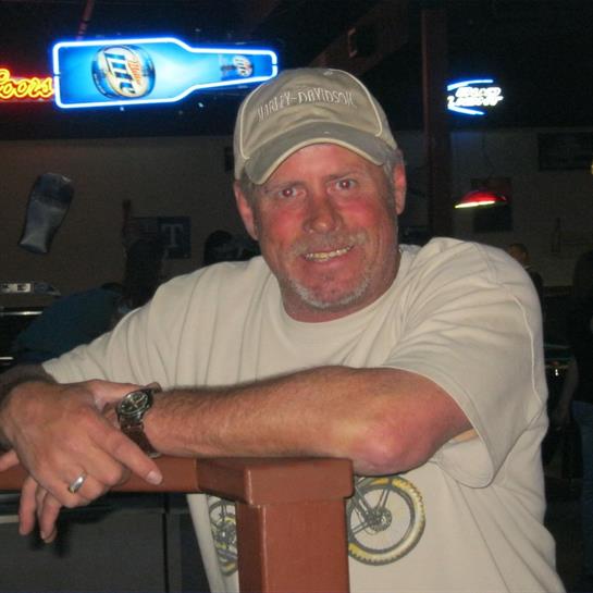 A man smiles at the bar, enjoying a relaxed moment with neon lights behind him.