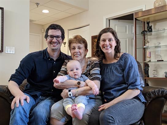 Four family members gather in a bright living room, sharing joyful moments with a baby.