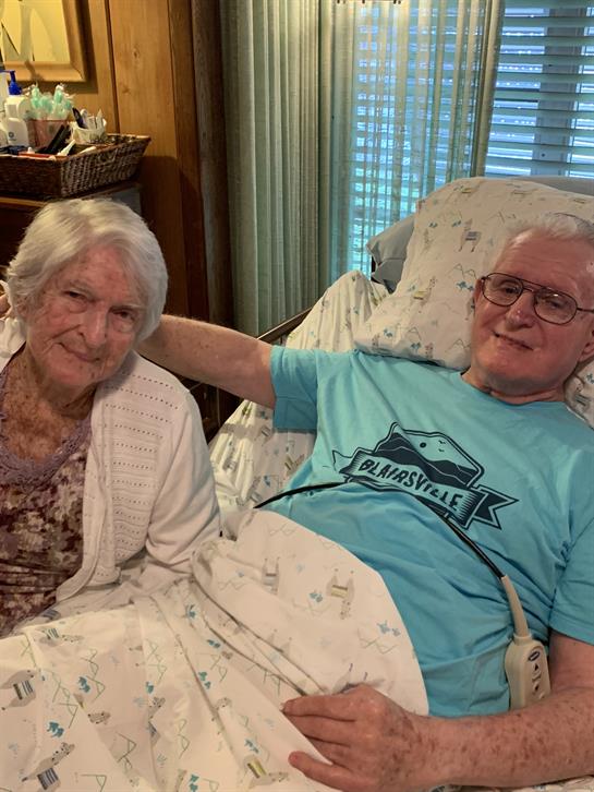 Two elderly individuals share a warm moment in a relaxed indoor environment while smiling.