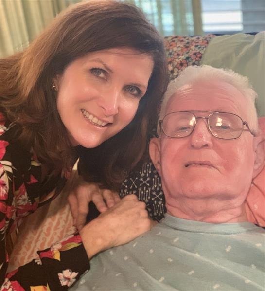 A woman smiles next to an older man indoors, sharing a warm moment together.