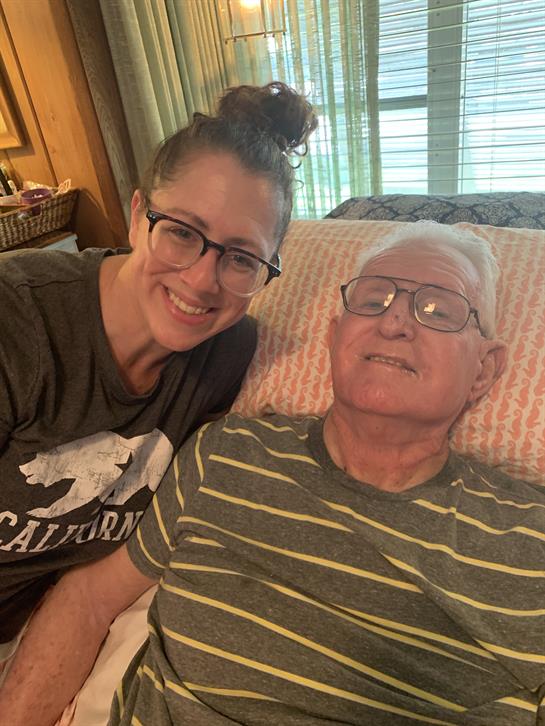 Caregiver smiles beside elderly man resting in bed, showcasing warmth and connection at home.