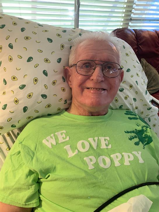 Senior man relaxes comfortably on bed, wearing a bright green shirt with a joyful expression.