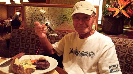An older gentleman is seated at a restaurant, happily holding a fork and enjoying his meal.