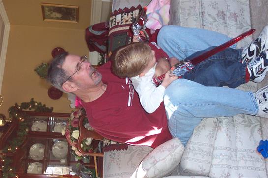 A man and a young boy are engaged in a joyful wrestling match on a sofa in a warm living room.
