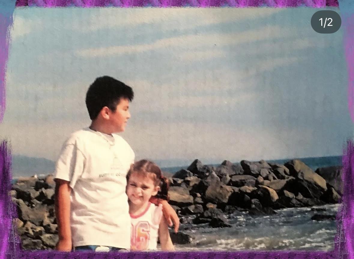 Two kids smile together at the water's edge, enjoying the beach view.