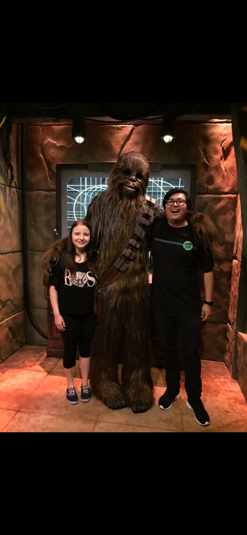 Two visitors smile while posing with a large, furry character at a themed attraction.