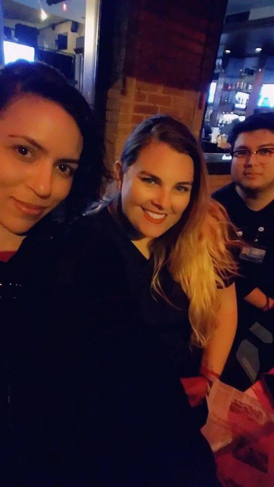 Three friends smile and pose together at a cozy bar during a lively night out in the city.
