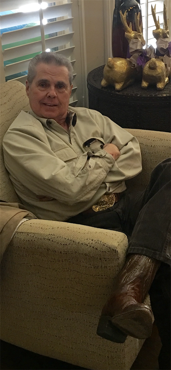 A man in a light shirt sits back in a chair, relaxed and engaged in conversation.