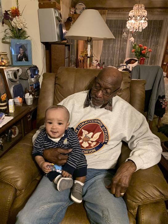 A joyful elderly man sits in an armchair with a happy baby on his lap at a family gathering.