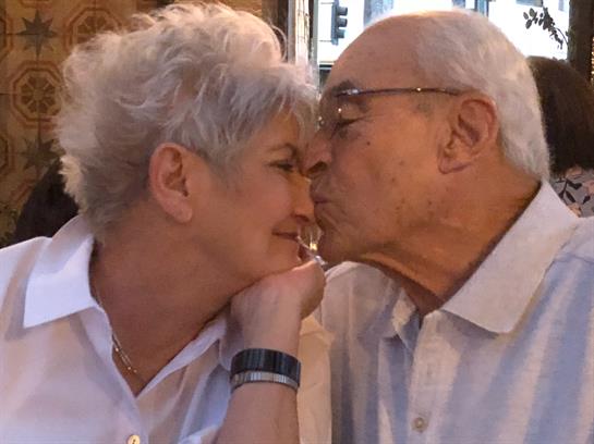 Two elderly individuals share a loving kiss while enjoying their time together in a café.