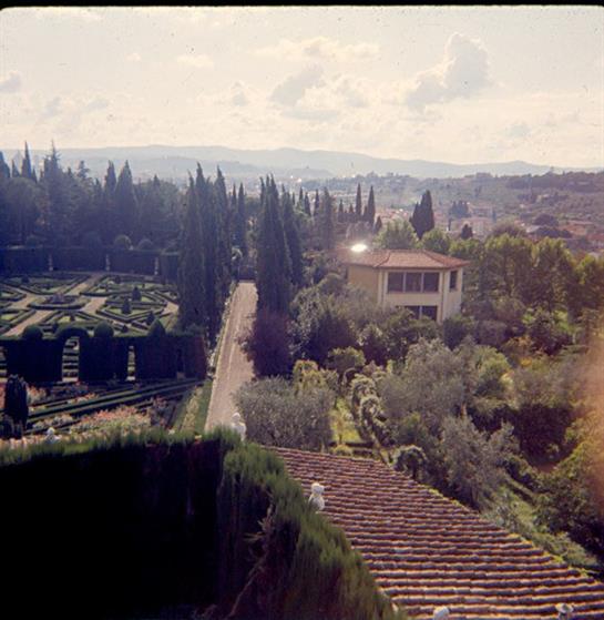 A peaceful countryside scene features manicured gardens and a road under a bright sky.