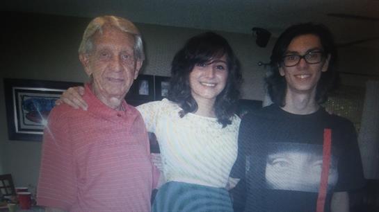 Three people stand close together, smiling happily in a warm atmosphere while wearing casual attire.