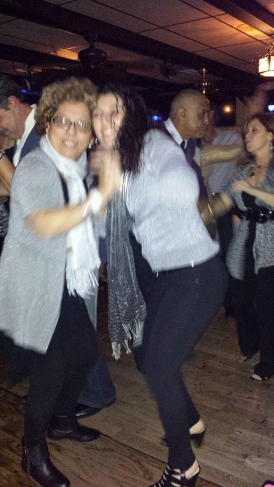 Two women dance joyfully at a festive gathering, surrounded by people in a vibrant atmosphere.