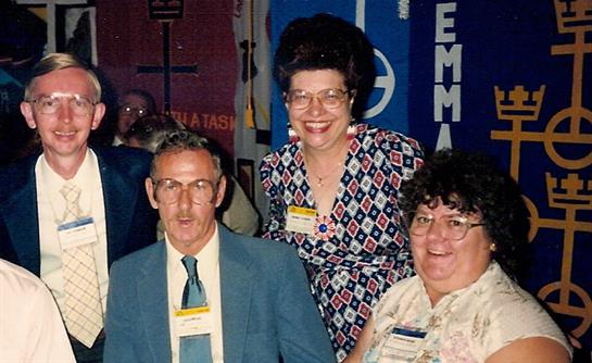 Three individuals share smiles at a community event in a vibrant venue filled with banners.