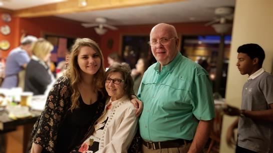 Three individuals pose happily in a vibrant social setting filled with activity and conversation.