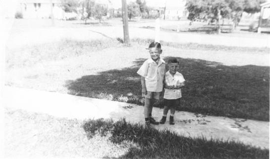 Two boys are standing on a path in a grassy area, enjoying their time outdoors together.