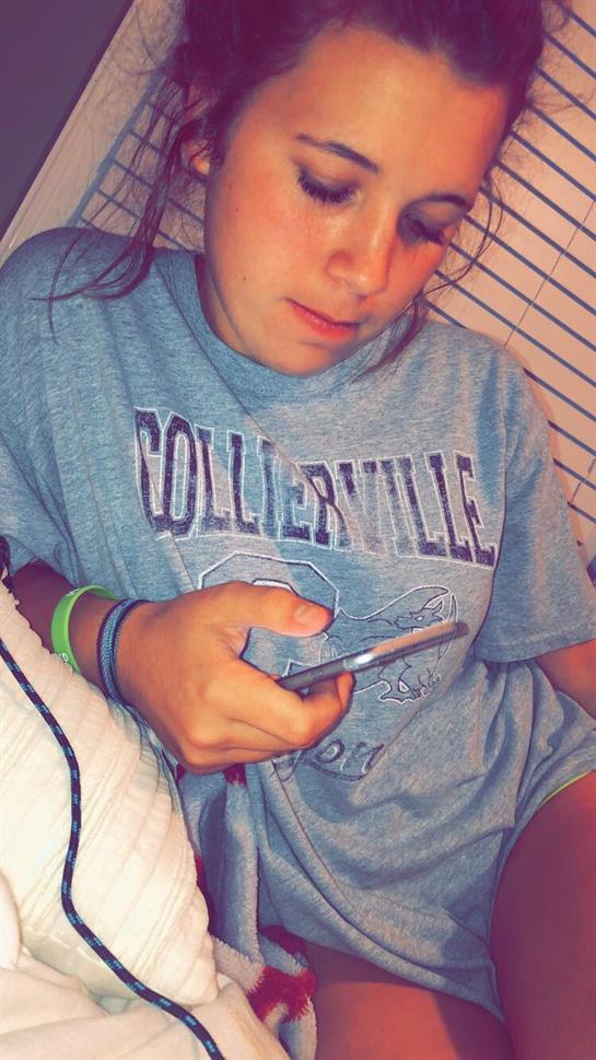 Individual relaxes at home, using a smartphone and wearing a comfortable oversized shirt.