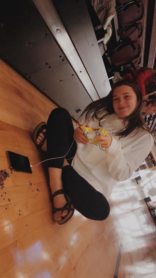 Young girl snacks and uses her phone, relaxing on a wooden floor in a cozy setting.