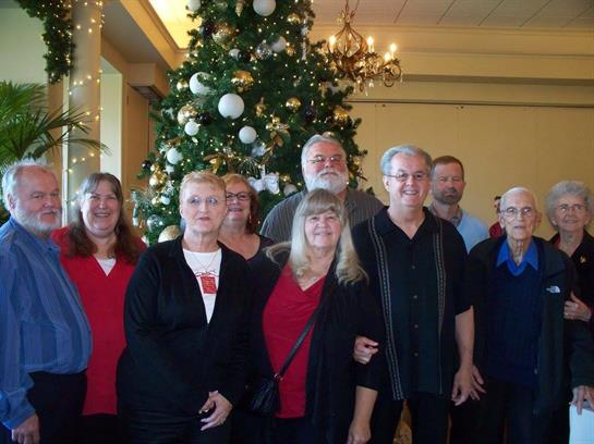 Group of family members posing together in festive attire by a large Christmas tree.