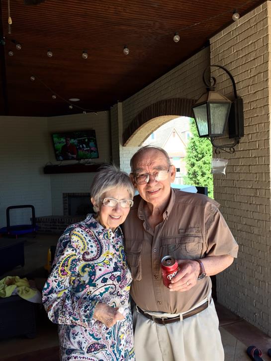 An elderly couple shares a warm smile together outdoors at home.