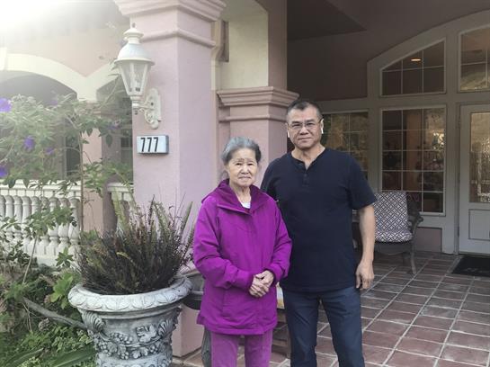 Two family members stand together outside a welcoming residence during dusk.