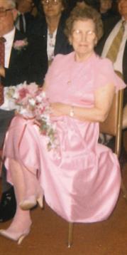 A woman wearing a pink dress sits elegantly, holding a bouquet of flowers during a special event.