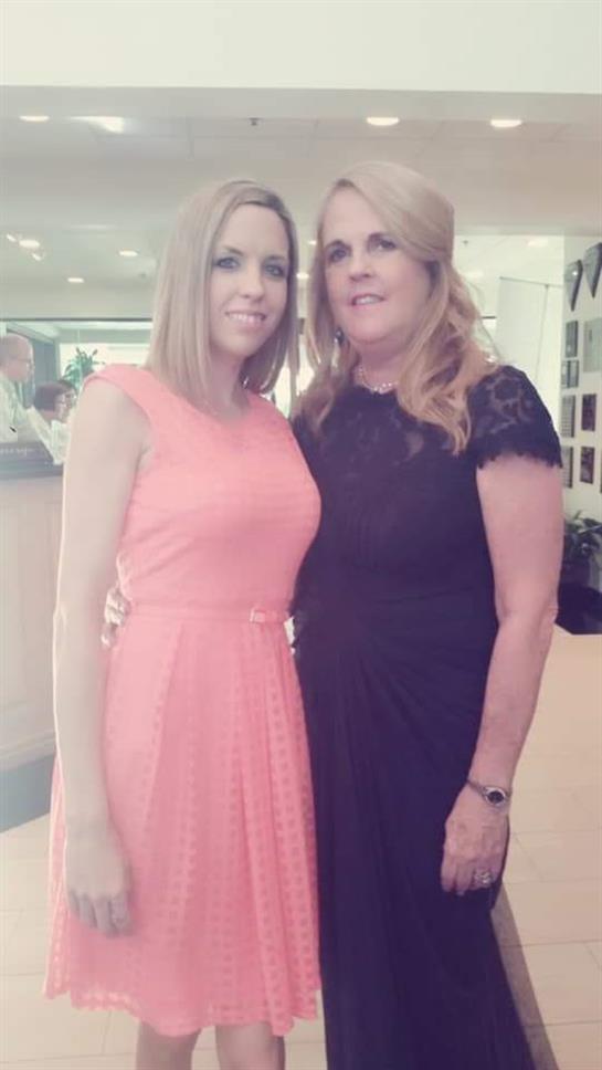 A joyful gathering shows a young woman in pink and a middle-aged woman in black, posing.