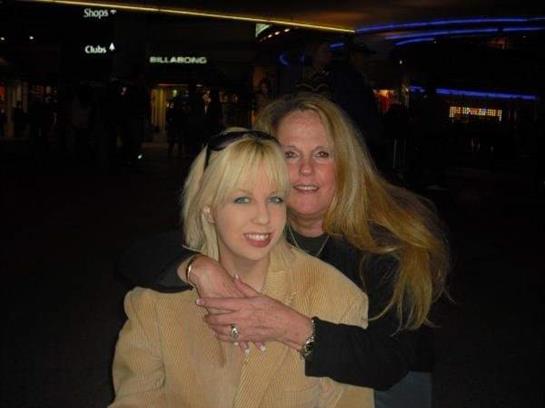 Two women smile warmly while embracing each other in a vibrant nightlife environment.