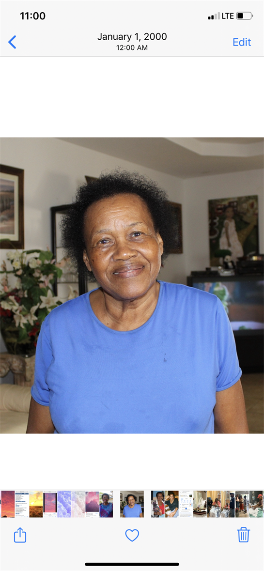 An elderly woman stands in her living room, smiling.