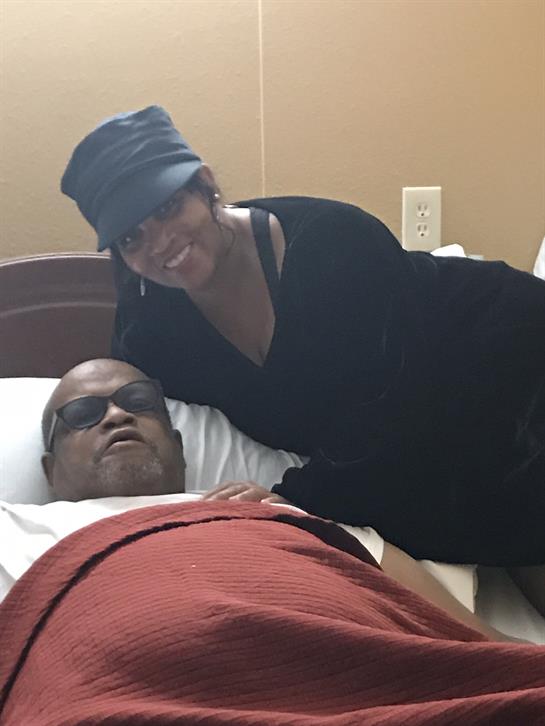 A woman smiles while visiting a man in a hospital room, showcasing a moment of support and care.