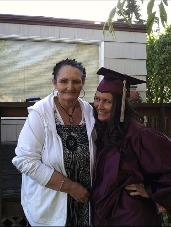 Two women smile together after a graduation ceremony in a backyard setting.