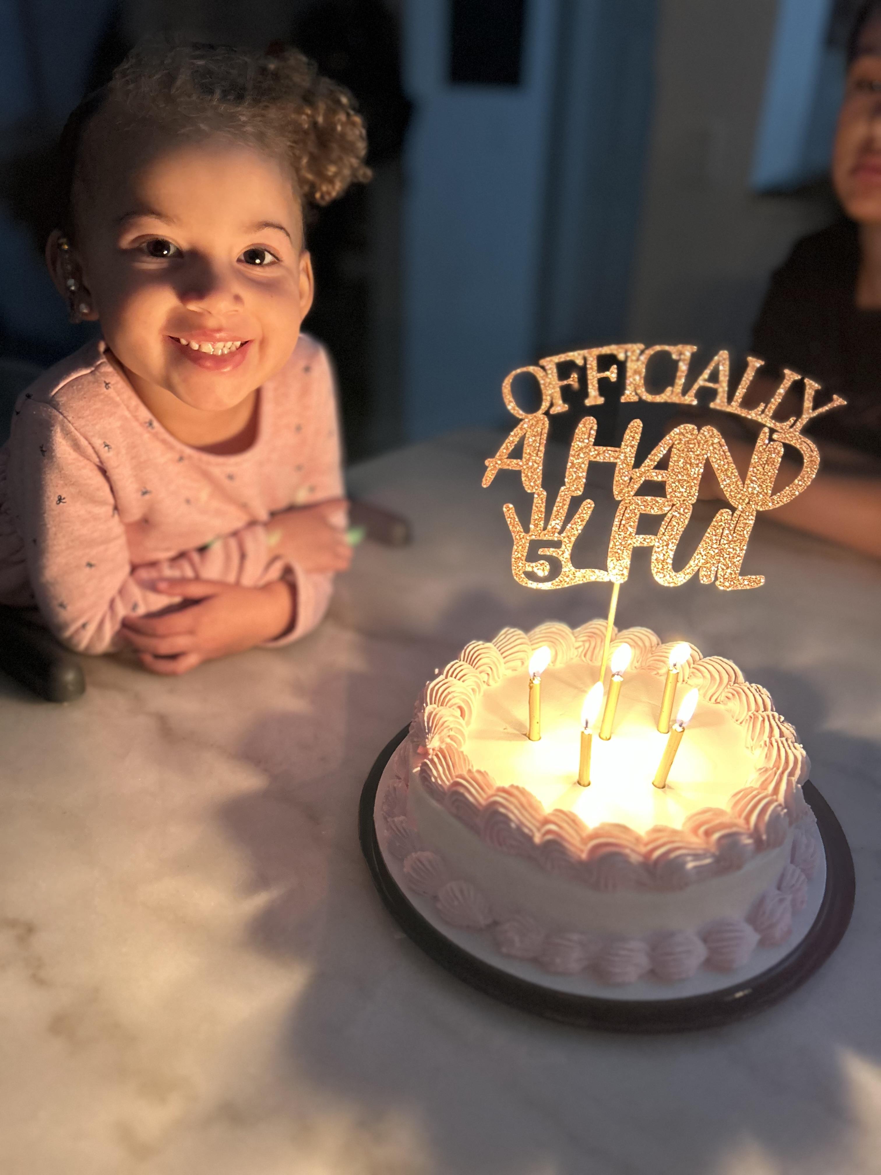 Joyful child celebrates turning five with a decorated cake and glowing candles.