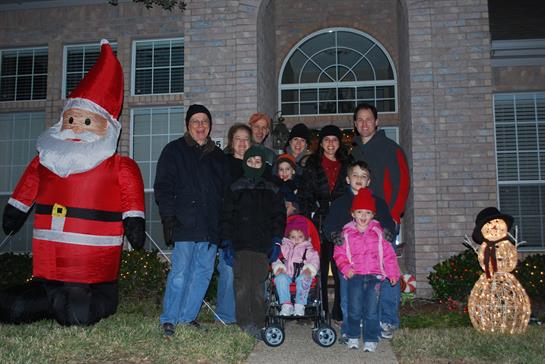 Family members pose joyfully outside a cozy house with festive decorations, celebrating together.